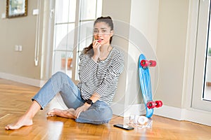 Young woman sitting on the floor using skateboard and headphones looking stressed and nervous with hands on mouth biting nails