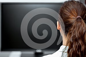 Young woman sitting in front of a black monitor or tv, backview