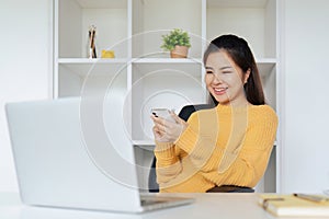 Young woman sitting in front of computer laptop and using mobile phone