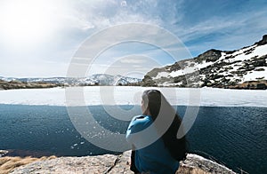 Young woman sitting in front of a Frozen lake in the top of snowy mountains