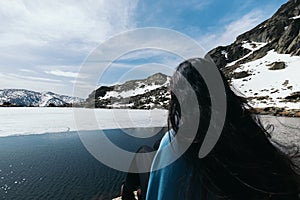 Young woman sitting in front of a Frozen lake in the top of snowy mountains. Close-up