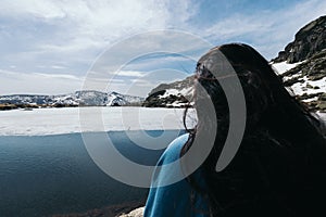 Young woman sitting in front of a Frozen lake in the top of snowy mountains. Close-up