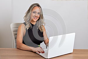 Young woman sitting in front of a notebook, hands on the keyboard and smiling at the viewer.  on white background