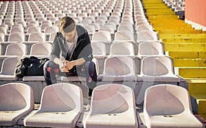 A young woman is sitting on the grandstand and taking a rest after a training at the stadium. Sport, athletics, athletes