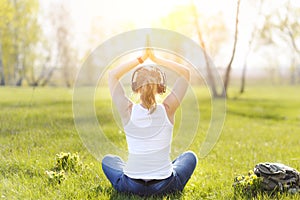 Young woman sitting on grass in Park and meditating and listening to music on headphones.