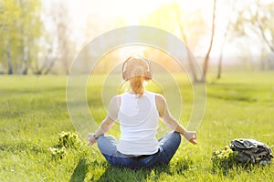 Young woman sitting on grass in Park and meditating and listening to music on headphones.