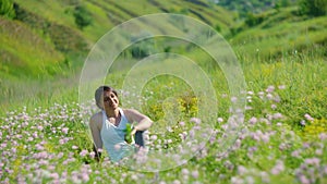 Young woman sitting in green grass meadow and wild flowers enjoying spring summer sunlight