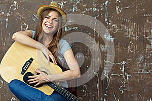 Young woman sitting with guitar on grunge wall background.