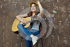 Young woman sitting with guitar on grunge wall background.