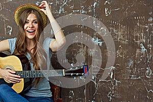 Young woman sitting with guitar on grunge wall background.