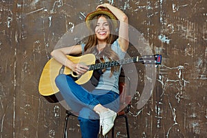 Young woman sitting with guitar on grunge wall background.