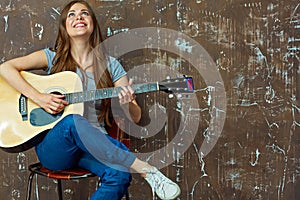 Young woman sitting with guitar on grunge wall background.