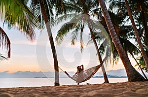 Young woman sitting in hammock swinging on the exotic island sand beach at sunrise time