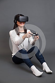 Young woman sitting and having fun playing a virtual reality video game against a dark background