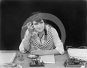 Young woman sitting at her desk in an office with a telephone in her hands