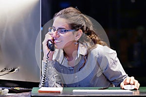 Young woman sitting at her desk working and answering a phone call.