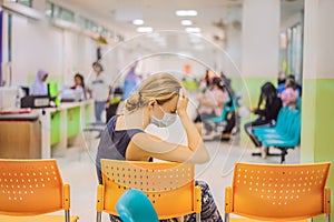 Young woman sitting in hospital waiting for a doctor`s appointment. Patients In Doctors Waiting Room
