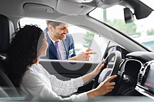 Young woman sitting inside car, having conversation with sales manager