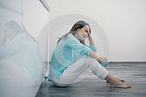 Young woman sitting on kitchen floor holding her head and crying, upset, sad, depressed