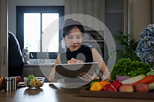 Young woman sitting in the kitchen and using digital tablet for recipes online