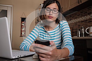 Young woman sitting in kitchen and working on laptop in morning. Female using laptop dining table