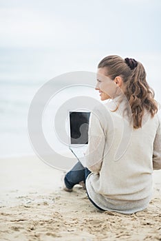 Young woman sitting with laptop on cold beach