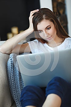 Young woman sitting with laptop on sofa at her home