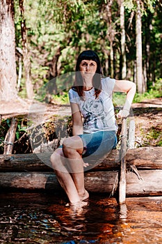 Young woman sitting on logs and lowered her feet into the river.