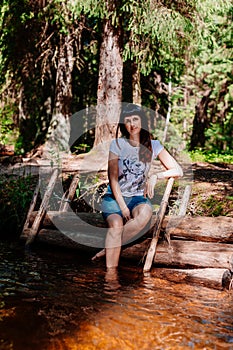 Young woman sitting on logs and lowered her feet into the river.