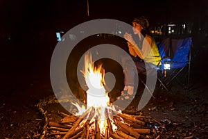 Young woman sitting near the campfire at night