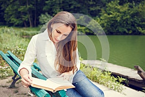 Young woman sitting near pond and reading book