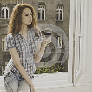 Young woman sitting near window with a glass of wine