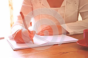 Young woman sitting near window and writing. retro filtered image. photograph with natural window light . sekective focus