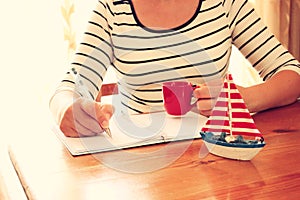 Young woman sitting near window and writing. retro filtered image. photograph with natural window light . selective focus