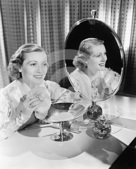 Young woman sitting next to mirror and holding a powder puff