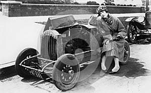 Young woman sitting next to small car looking at the engine in disbelieve