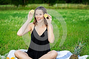 Young woman sitting outdoors and holding sliced lemon