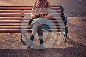 Young woman sitting on park bench with book