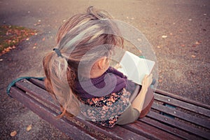 Young woman sitting on park bench with book