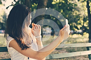 Young woman sitting on a park bench and photographed on a mobile