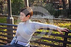 The young woman is sitting on a park bench in Rome.