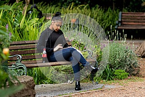 Young woman sitting on park bench using a tablet or phone before Covid