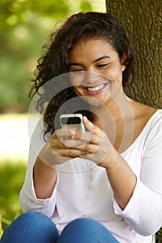 Young Woman Sitting In Park Sending Text Message