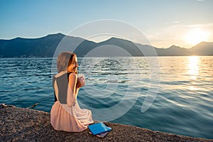 Young woman sitting on the pier at sunrise