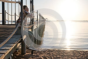 Young Woman sitting on a pier in sunrise, enjoying the view