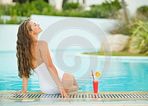 Young woman sitting at poolside with cocktail