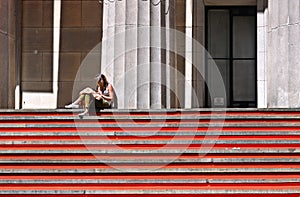 Young woman sitting and reading book on red stairs in front of Federal Hall in front the front, wall street, Manhattan, New York C