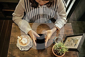 young woman sitting in restaurant and using mobile phone has coffee cup with latte art and place on wooden table background