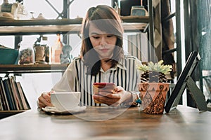 Young woman sitting in restaurant and using mobile phone has cup