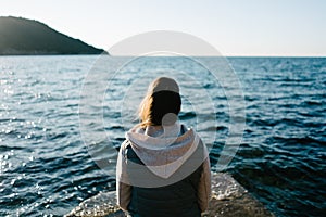 Young woman sitting on a rock, gazing in the distance, looking in the sea.